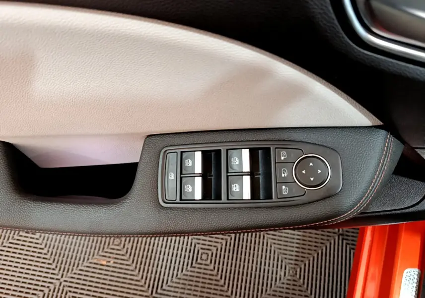 Gros plan sur la commande des vitres côté conducteur de la Renault Clio Initiale Paris orange, avec surpiqûres rouges.