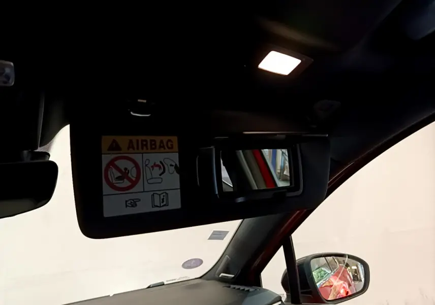 Détail intérieur du pare-soleil côté conducteur avec miroir et avertissement airbag, reflet orange Renault Clio visible au rétroviseur.