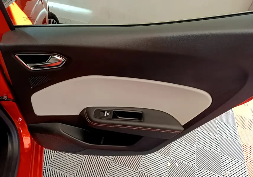 Vue intérieure côté gauche de la porte avant orange de la Renault Clio Initiale Paris E-TECH 140 avec garniture bicolore noire et beige.