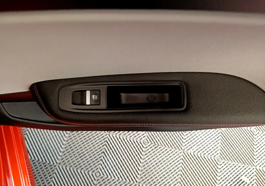 Gros plan sur la poignée intérieure et le bouton de verrouillage de la porte côté gauche d'une Renault Clio Initiale Paris orange.