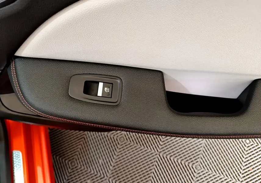 Gros plan sur la commande de lève-vitre côté conducteur, garniture noire avec surpiqûres orange, intérieur Renault Clio orange.