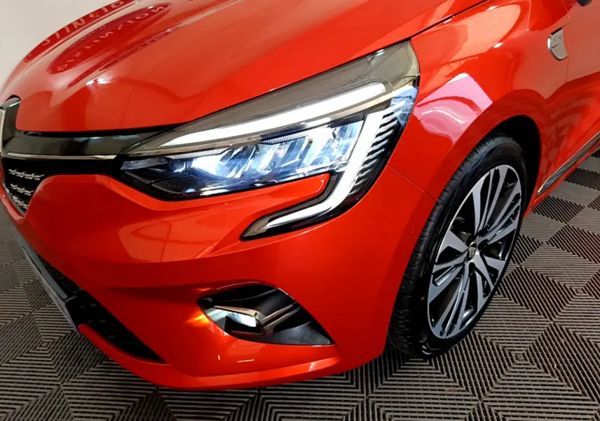 Gros plan sur l'avant droit de la Renault Clio Initiale Paris orange, mettant en valeur le phare LED et la jante alliage.