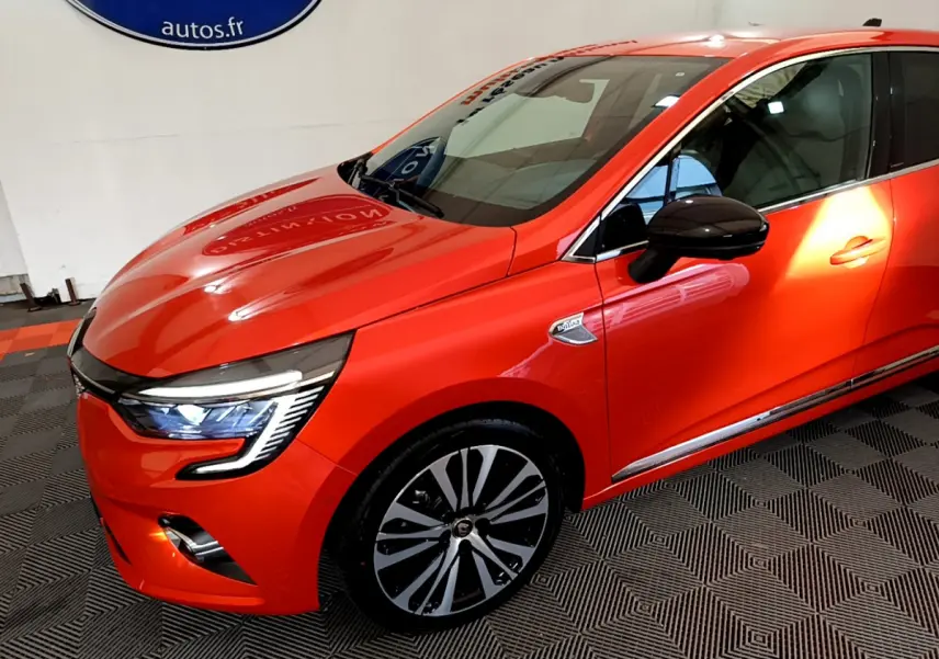 Vue 3/4 avant droite d'une Renault Clio Initiale Paris orange avec phares LED et jantes alliage distinctives.