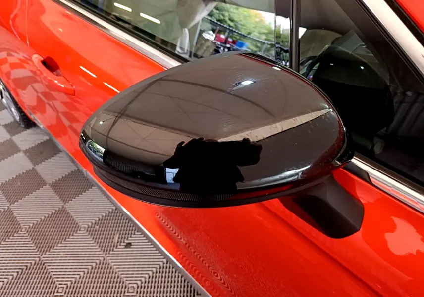 Rétroviseur noir côté gauche sur porte orange vif d'une Renault Clio Initiale Paris E-TECH 2021 vue rapprochée.