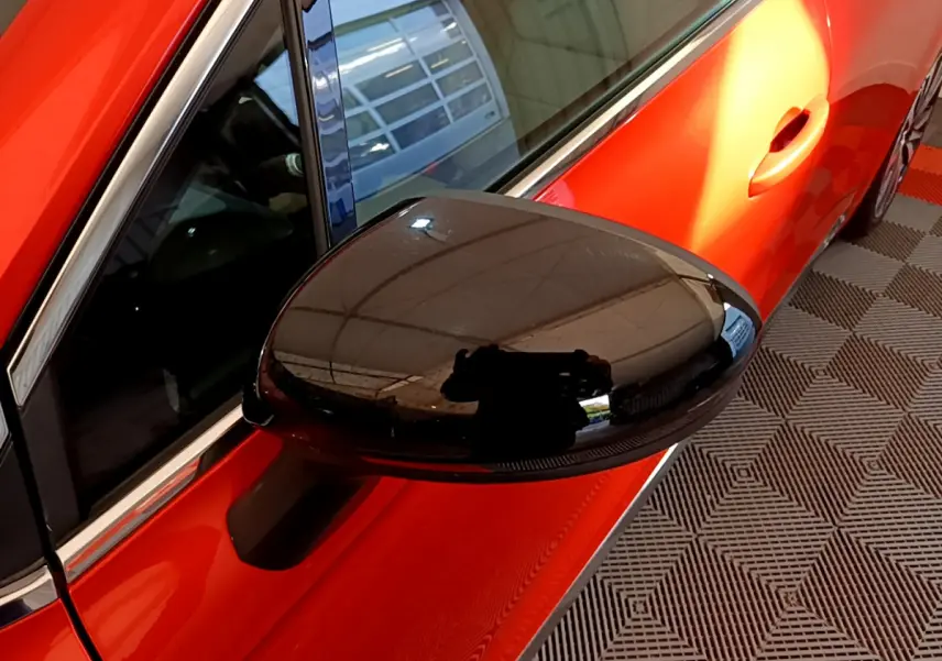 Rétroviseur noir en gros plan côté gauche sur une Renault Clio Initiale Paris orange vue de profil partiel.