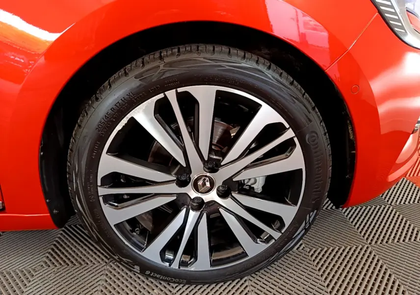 Gros plan sur la roue avant gauche d'une Renault Clio orange 2021 avec jante alliage bicolore et logo Renault au centre.