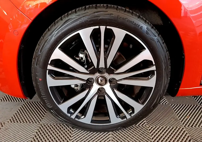 Gros plan sur la roue avant droite de la Renault Clio Initiale Paris orange, mettant en valeur la jante alliage bicolore et le logo Renault.