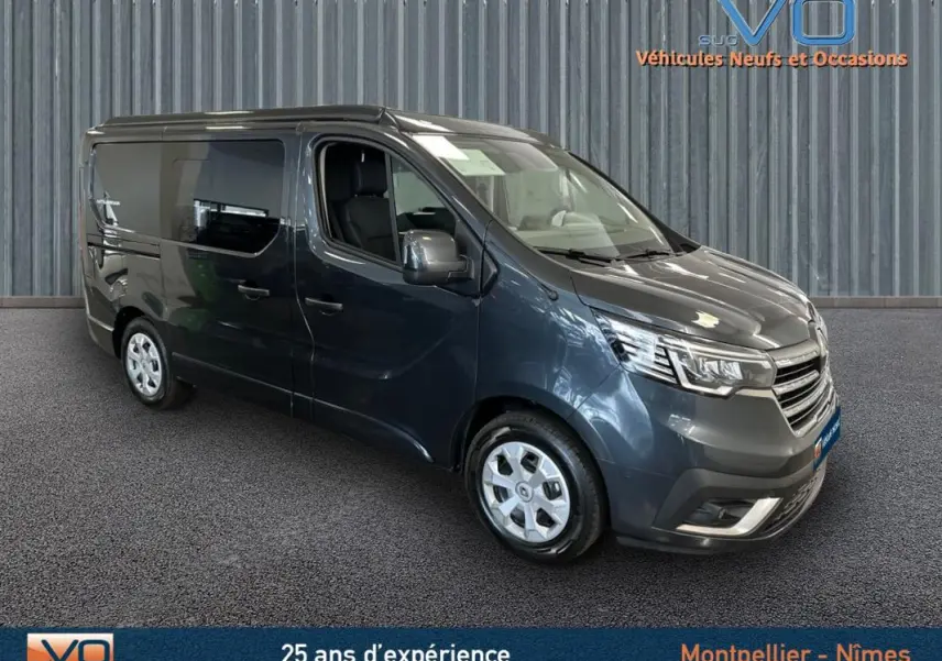 Renault Trafic Fourgon gris en 3/4 avant droit, vitres surteintées et jantes alliage visibles en intérieur showroom.