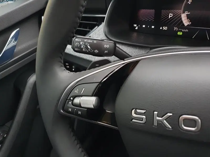 Gros plan sur le volant cuir noir du Skoda Kamiq gris, avec commandes audio et tableau de bord numérique en arrière-plan.