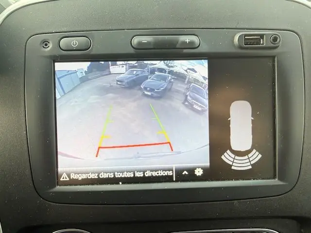 Écran de caméra de recul montrant une vue arrière avec lignes de guidage colorées et plusieurs véhicules stationnés.