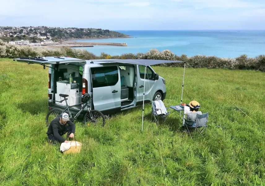 Renault Trafic Fourgon gris platine vu de côté droit arrière, porte coulissante ouverte et auvent déployé.