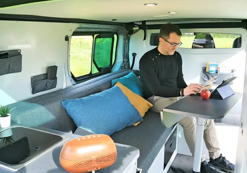 Intérieur du Renault Trafic Fourgon gris platine, vue latérale montrant banquette, table et aménagement compact.