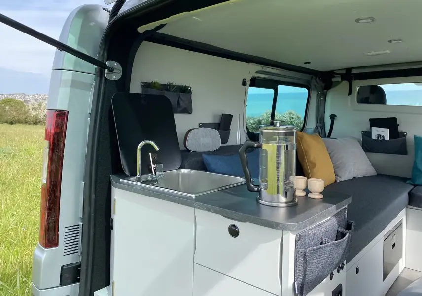 Intérieur du Renault Trafic gris platine, vue arrière ouverte montrant cuisine compacte avec évier et espace détente aménagé.