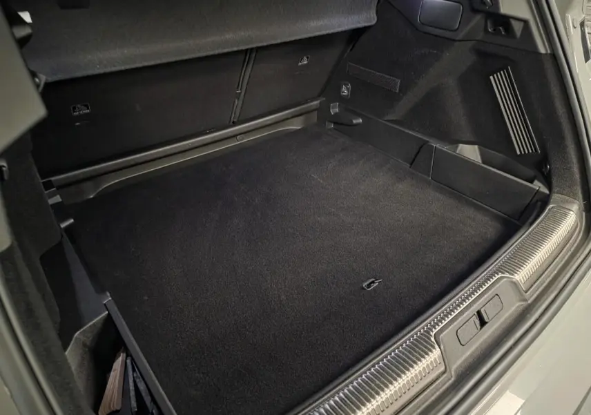 Coffre ouvert du DS7 Crossback gris, montrant le tapis de sol noir et les rangements latéraux.
