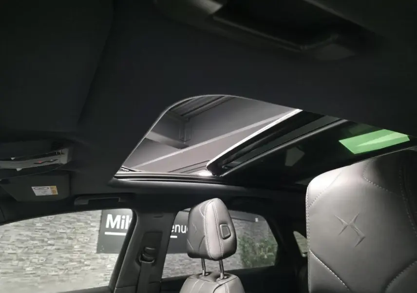 Intérieur du DS7 Crossback gris, vue sur les sièges avant en cuir noir avec toit ouvrant panoramique ouvert.