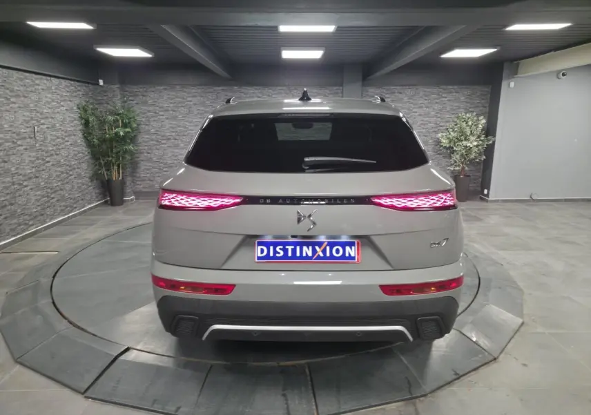 Vue arrière du DS7 Crossback gris avec feux arrière LED 3D et logo DS Automobiles sur fond intérieur showroom.