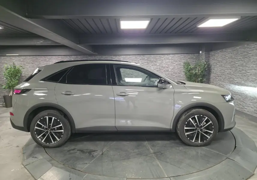 Vue de profil côté gauche du DS7 Crossback gris métallisé avec jantes alliage noires et toit noir en intérieur showroom.
