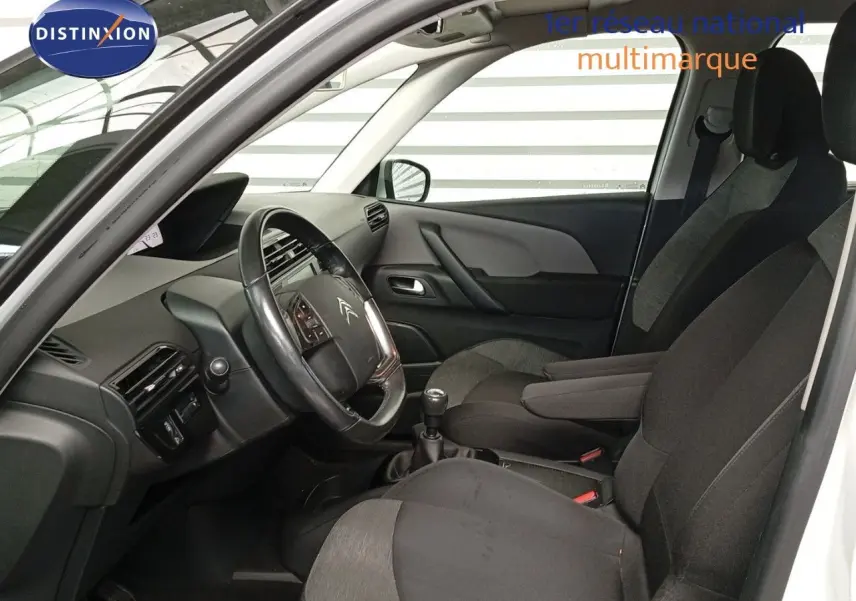 Intérieur avant du Citroën Grand C4 Picasso blanc 2016, vue côté conducteur avec volant et sièges tissu noir et gris.
