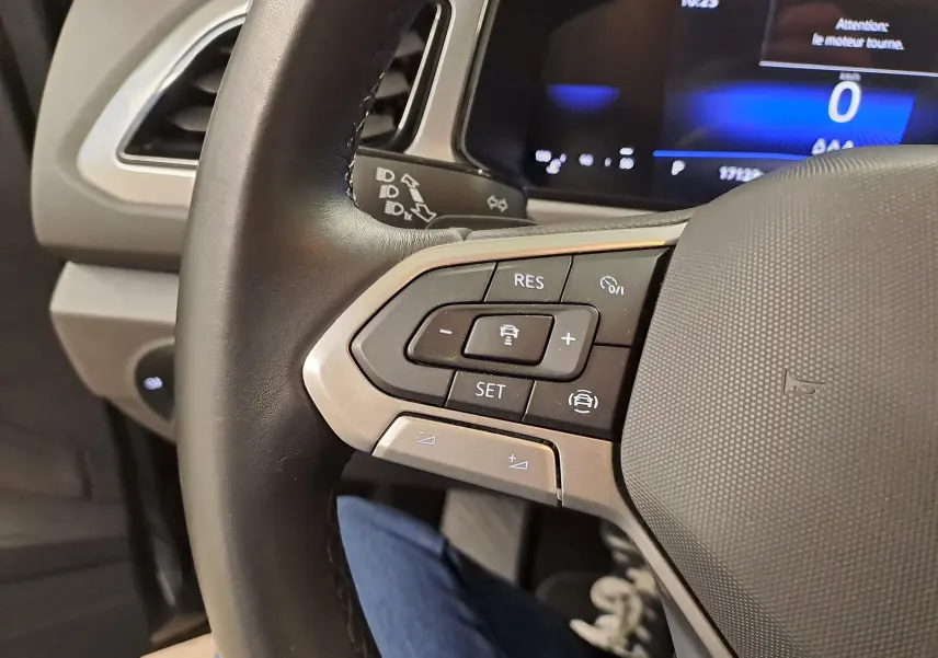 Gros plan sur les commandes du volant à gauche du Volkswagen T-Roc 2024, avec tableau de bord numérique en arrière-plan.