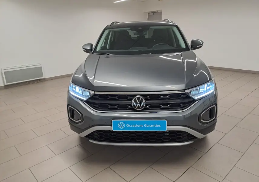 Volkswagen T-Roc 2024 gris Indium vue de face avec phares allumés et calandre noire hexagonale.