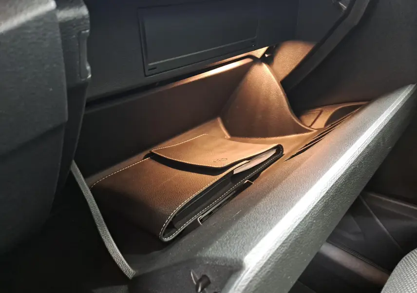 Gros plan sur la boîte à gants ouverte du Volkswagen T-Roc 2024, montrant un étui en cuir noir avec éclairage intérieur.