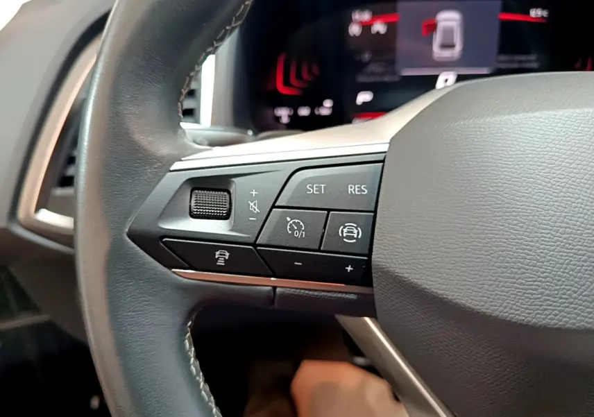 Gros plan sur les commandes du volant côté gauche du SEAT Ateca noir 2022, avec affichage numérique en arrière-plan.