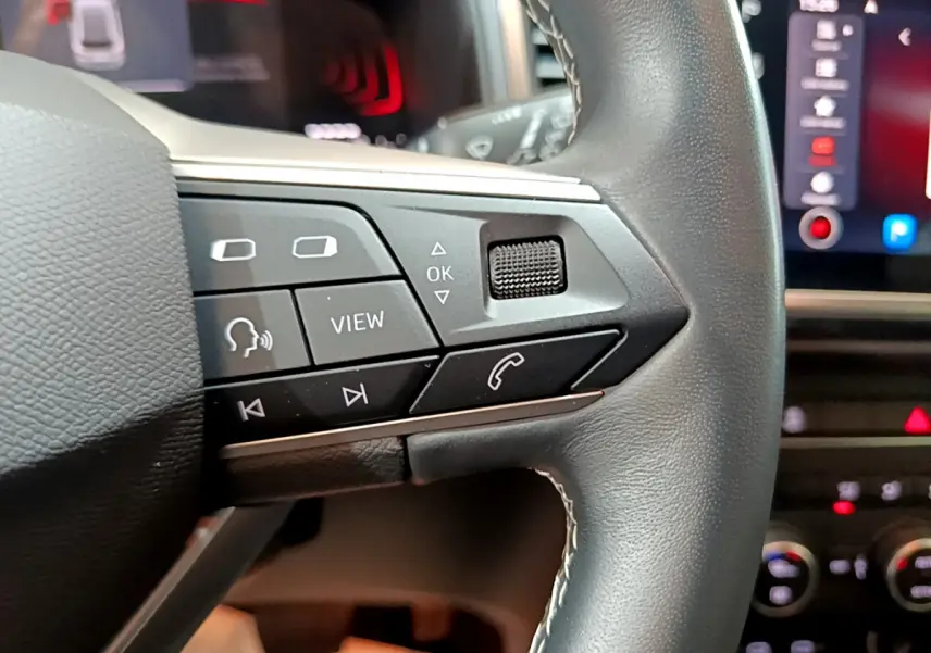 Gros plan sur les commandes du volant cuir noir du SEAT Ateca 2022, avec écran tactile et affichage digital en arrière-plan.