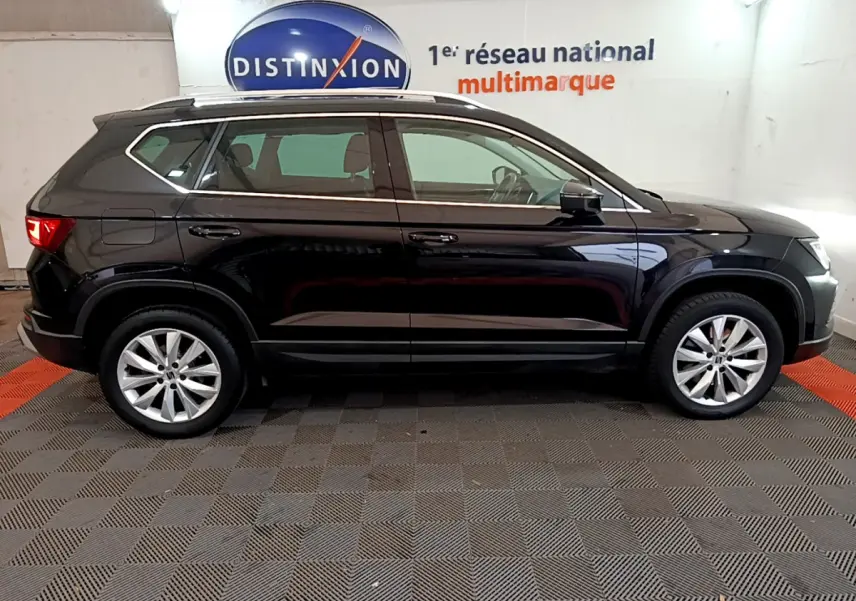 Profil côté droit d'un SUV SEAT Ateca noir 2022 dans un showroom avec jantes alliage et barres de toit chromées.