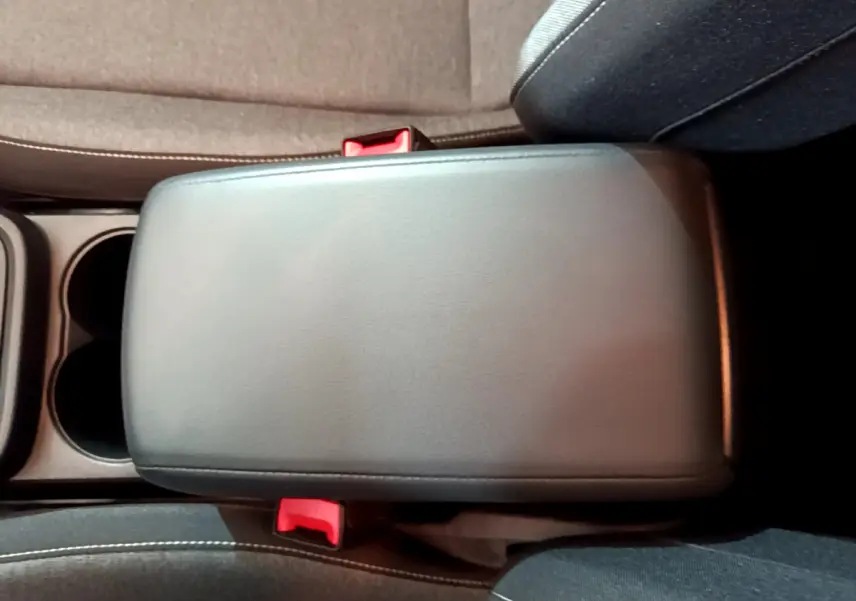 Accoudoir central noir vu de dessus entre sièges avant gris foncé avec ceintures de sécurité rouges visibles