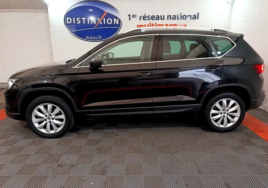 Vue latérale côté gauche d'un SUV SEAT Ateca noir 2022 garé en intérieur avec jantes alliage et barres de toit chromées.