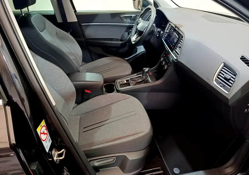 Vue intérieure côté conducteur du SEAT Ateca noir 2022, sièges tissu gris et tableau de bord avec écran tactile.