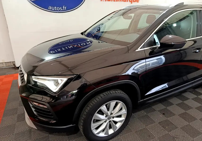 Vue 3/4 avant côté gauche d'un SEAT Ateca noir brillant avec jantes alliage et phares LED allumés en intérieur showroom.