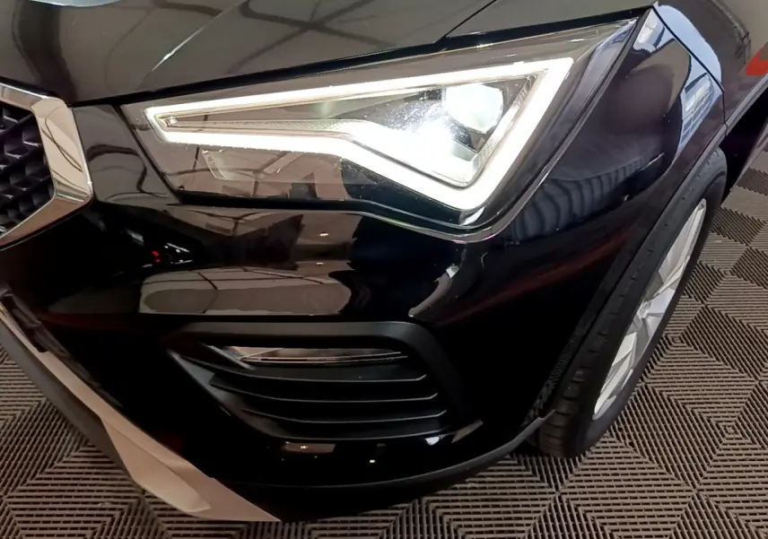 Gros plan sur le phare avant gauche allumé du SEAT Ateca noir, mettant en valeur la calandre et la roue avant.