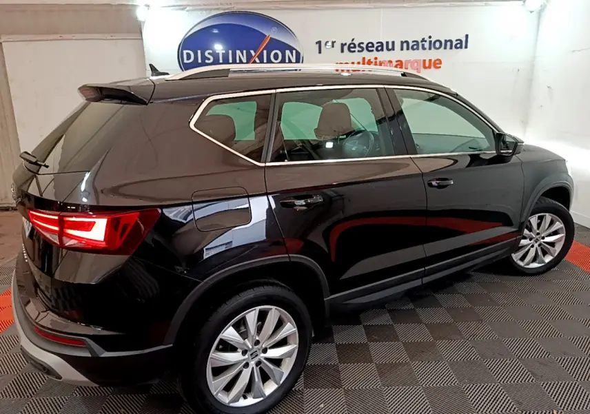 Vue 3/4 arrière côté gauche d'un SEAT Ateca noir avec feux arrière allumés et jantes alliage en showroom.