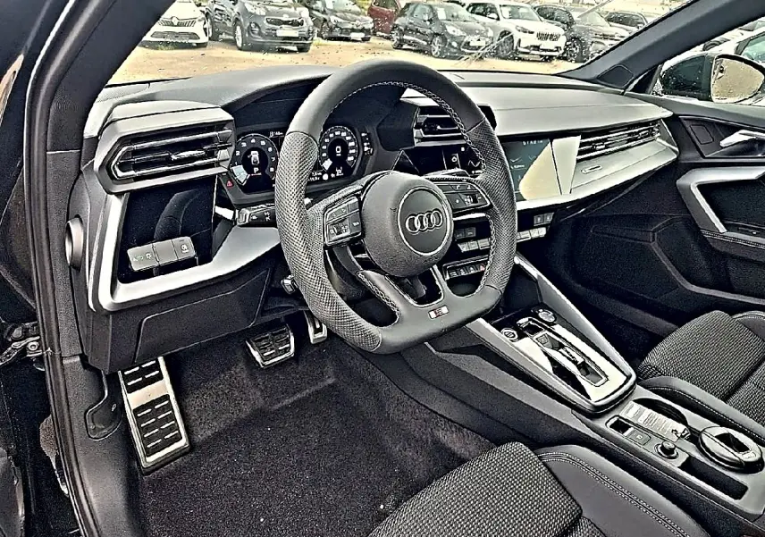 Vue intérieure côté conducteur de l'Audi A3 Sportback noir mythos, volant sport et tableau de bord digital visible.