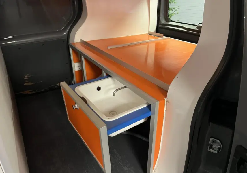 Vue intérieure côté gauche du Renault Kangoo Express 2016, montrant un meuble orange avec évier intégré dans l'espace de chargement.