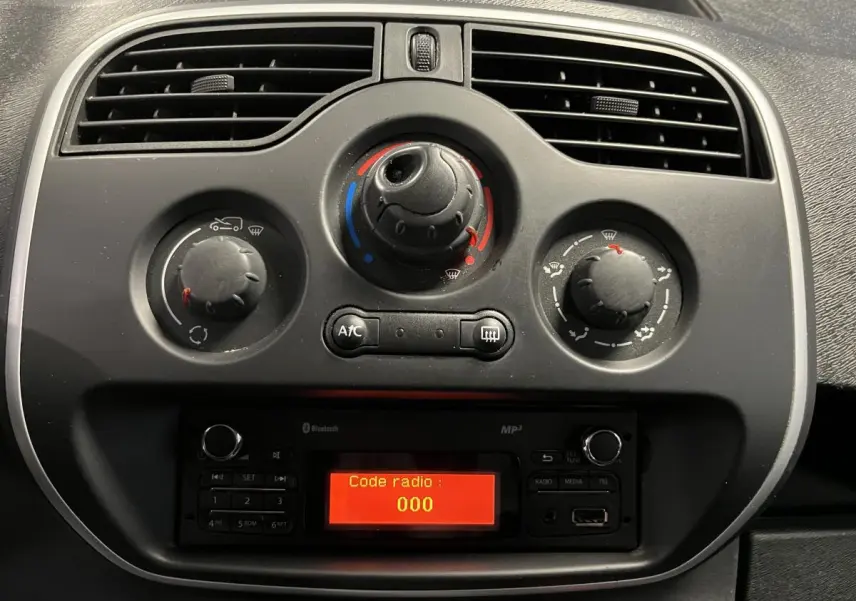 Gros plan sur la console centrale noire du Renault Kangoo Express gris foncé, avec commandes de climatisation et radio affichant "Code radio : 000"