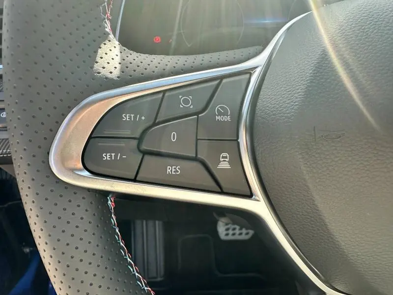 Gros plan sur les commandes du volant cuir perforé du Renault Captur 1.6 E-Tech esprit Alpine, avec surpiqûres tricolores.