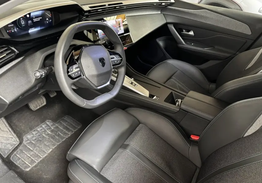 Intérieur noir de la Peugeot 308 PureTech 130 S&S Allure 2024, vue côté conducteur avec tableau de bord digital et volant cuir.