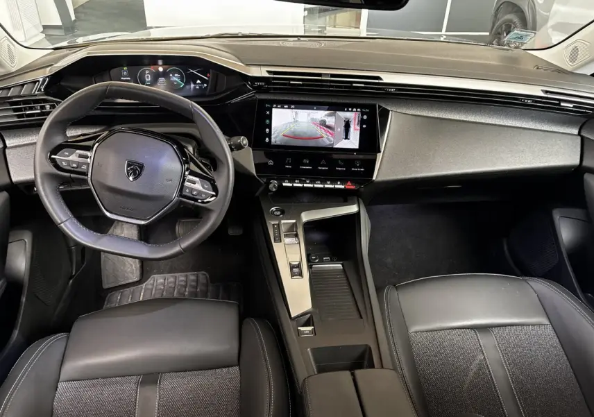 Vue intérieure avant de la Peugeot 308 gris clair, volant cuir, écran tactile affichant la caméra de recul.