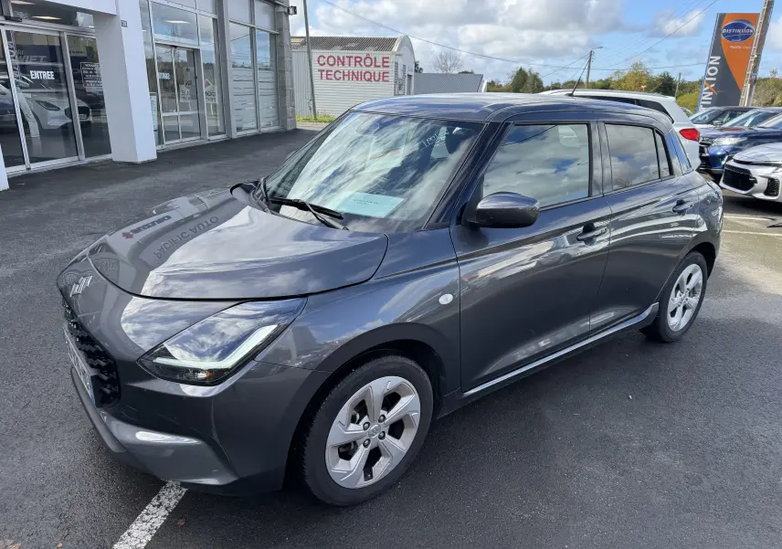 Suzuki Swift 1.2 Hybrid Privilege gris vue 3/4 avant droit, avec jantes alliage et calandre noire brillante.
