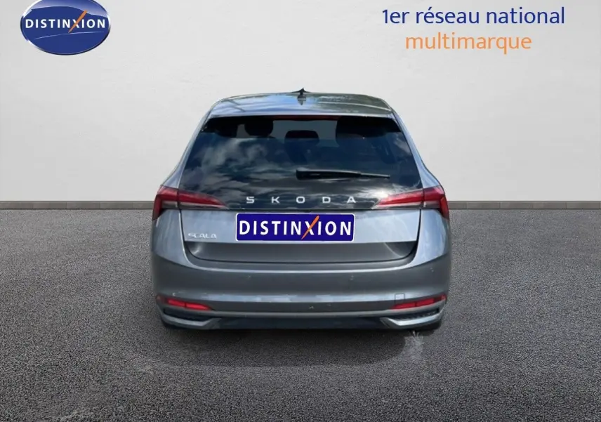 Vue arrière d'une Skoda Scala gris graphite métal, avec feux arrière allongés et hayon fermé sur sol gris.
