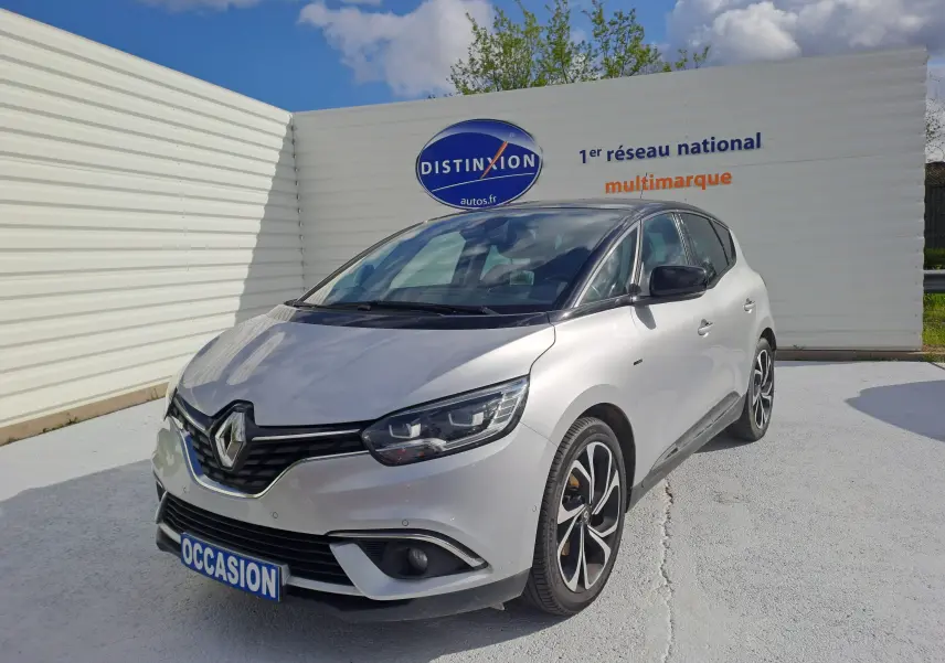 Renault Scénic IV gris platine avec toit noir, vue 3/4 avant droit, stationné devant un mur blanc.