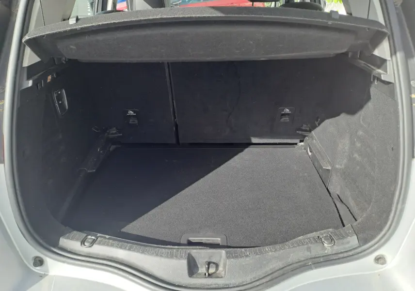 Coffre ouvert vu de l'arrière d'un Renault Scenic IV gris platine avec intérieur noir et cache-bagages relevé.