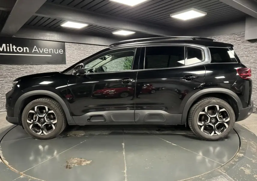 Profil latéral droit d'un Citroën C5 Aircross noir nacré avec jantes alliage bi-ton et barres de toit noires.