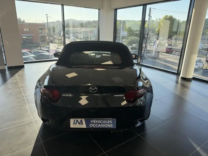 Vue arrière d'une Mazda MX-5 noire 1.5 SKYACTIV-G EUNOS EDITION 2020, capote fermée, en showroom lumineux.