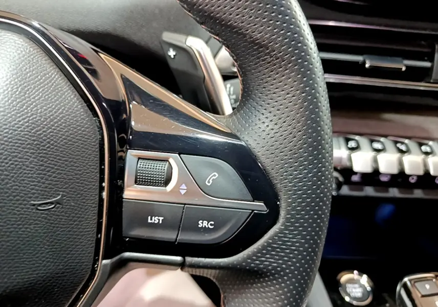 Gros plan sur le volant cuir perforé noir du Peugeot 3008 2023 avec commandes audio et palette de changement de vitesse.