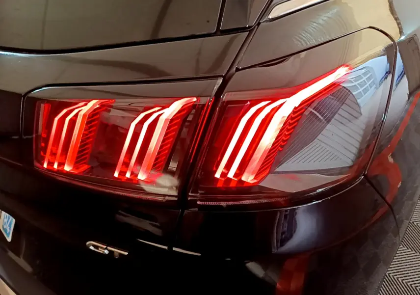 Gros plan sur le feu arrière droit rouge vif d’un Peugeot 3008 GT noir brillant de 2023.