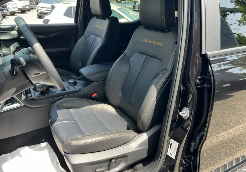Vue intérieure côté conducteur du Ford Ranger Wildtrak noir agate, sièges cuir avec surpiqûres orange et logo Wildtrak brodé.