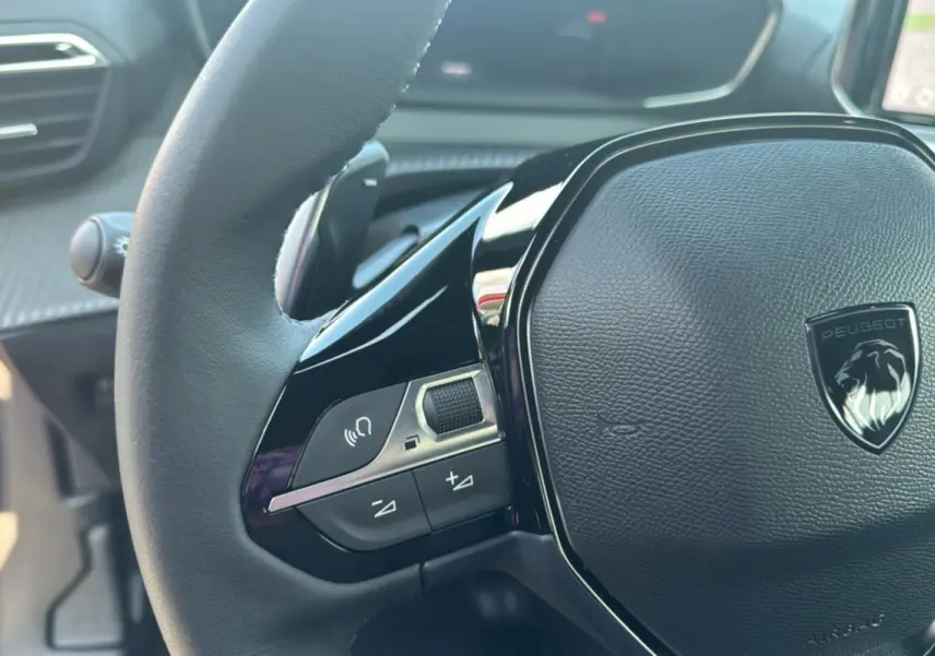 Gros plan sur le volant cuir noir multifonctions du Peugeot 2008 Hybrid 145, avec logo lion argenté au centre.